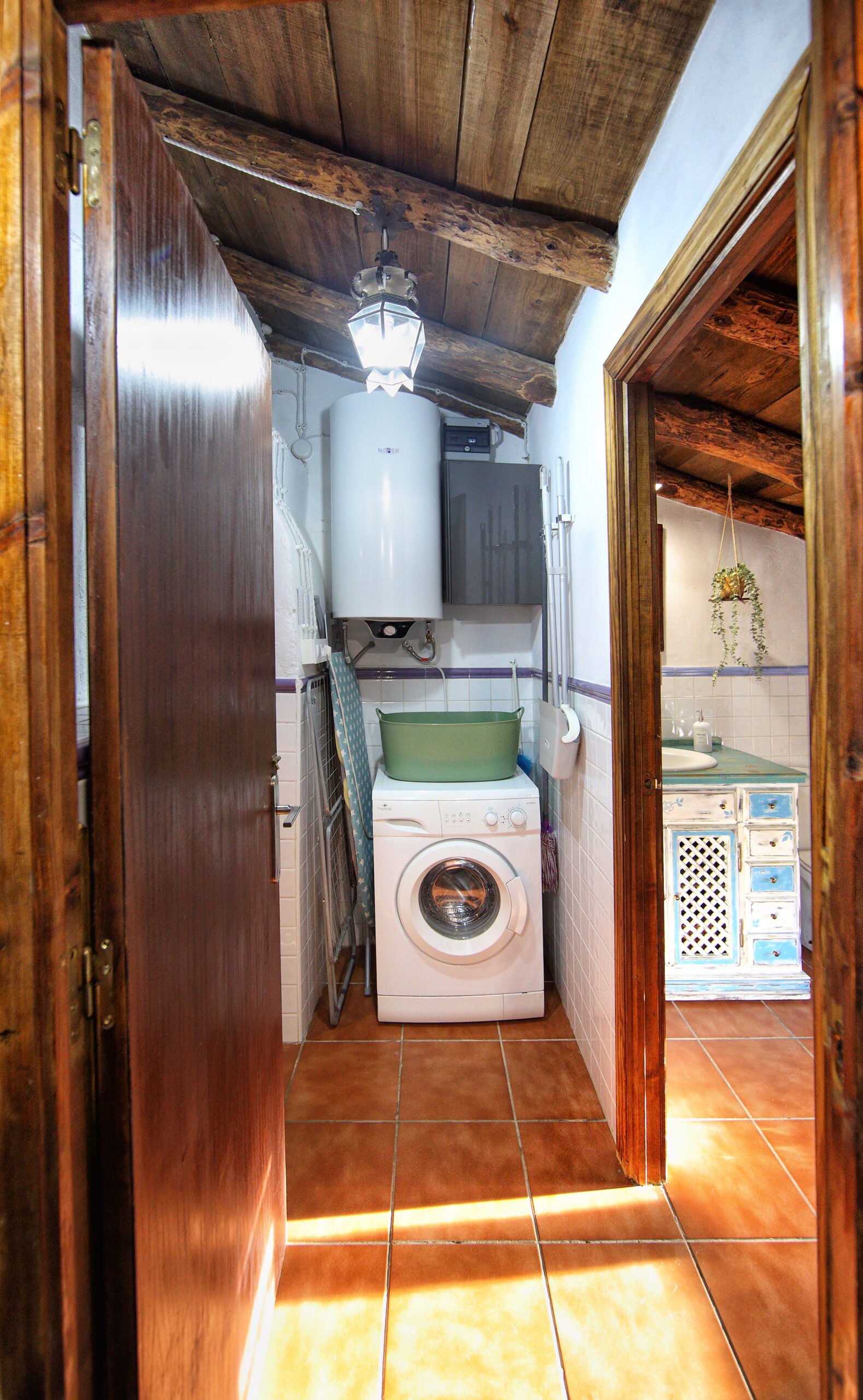 Zona de Lavandería y Serviciosç Cuarto de lavandería rústico con lavadora blanca, termo eléctrico y techos de madera en el Mirador de Santa Ana.