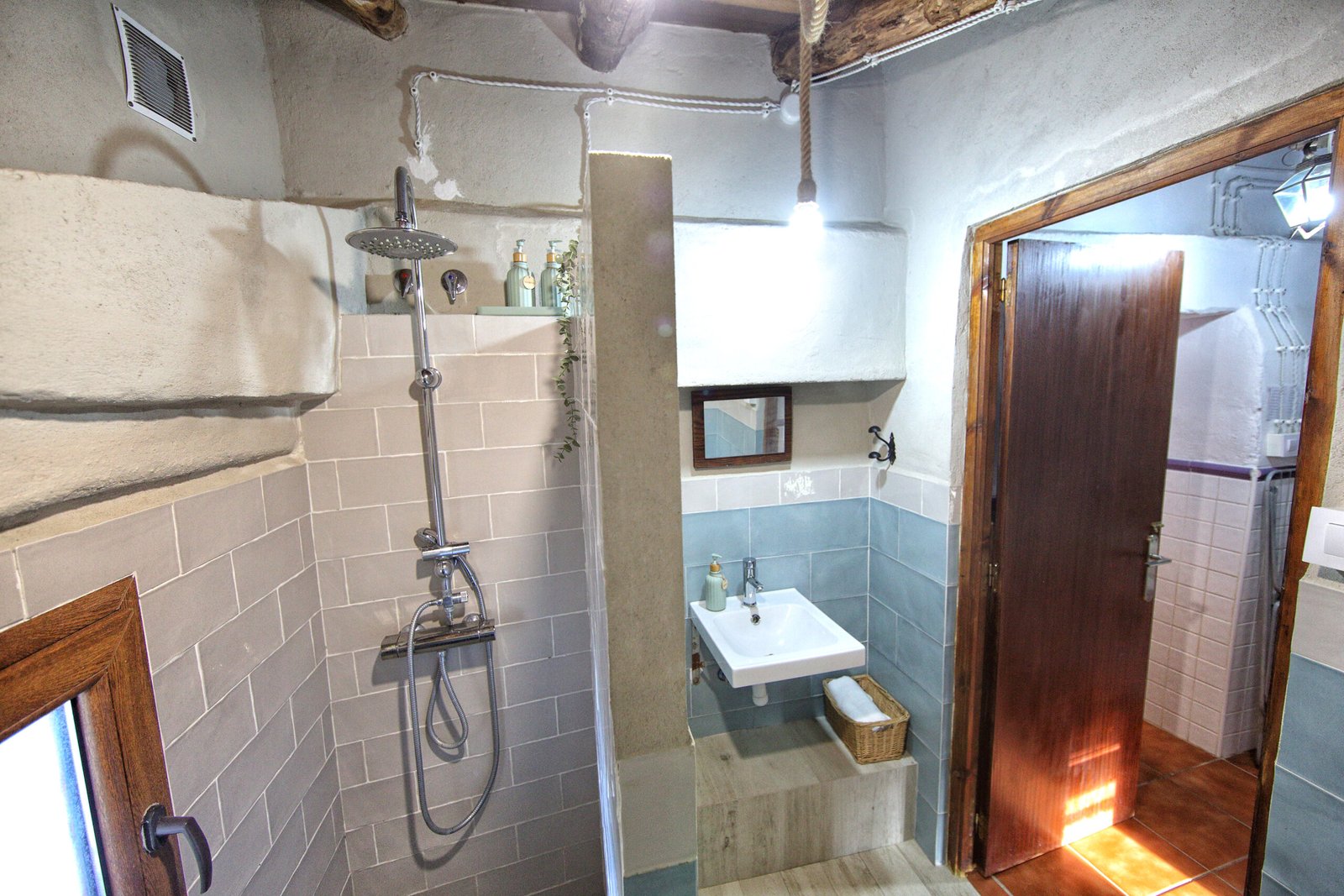 Baño Moderno Rústico con Ducha Interior de baño rústico con ducha moderna, lavabo pequeño, paredes de piedra clara y vigas de madera en el techo.