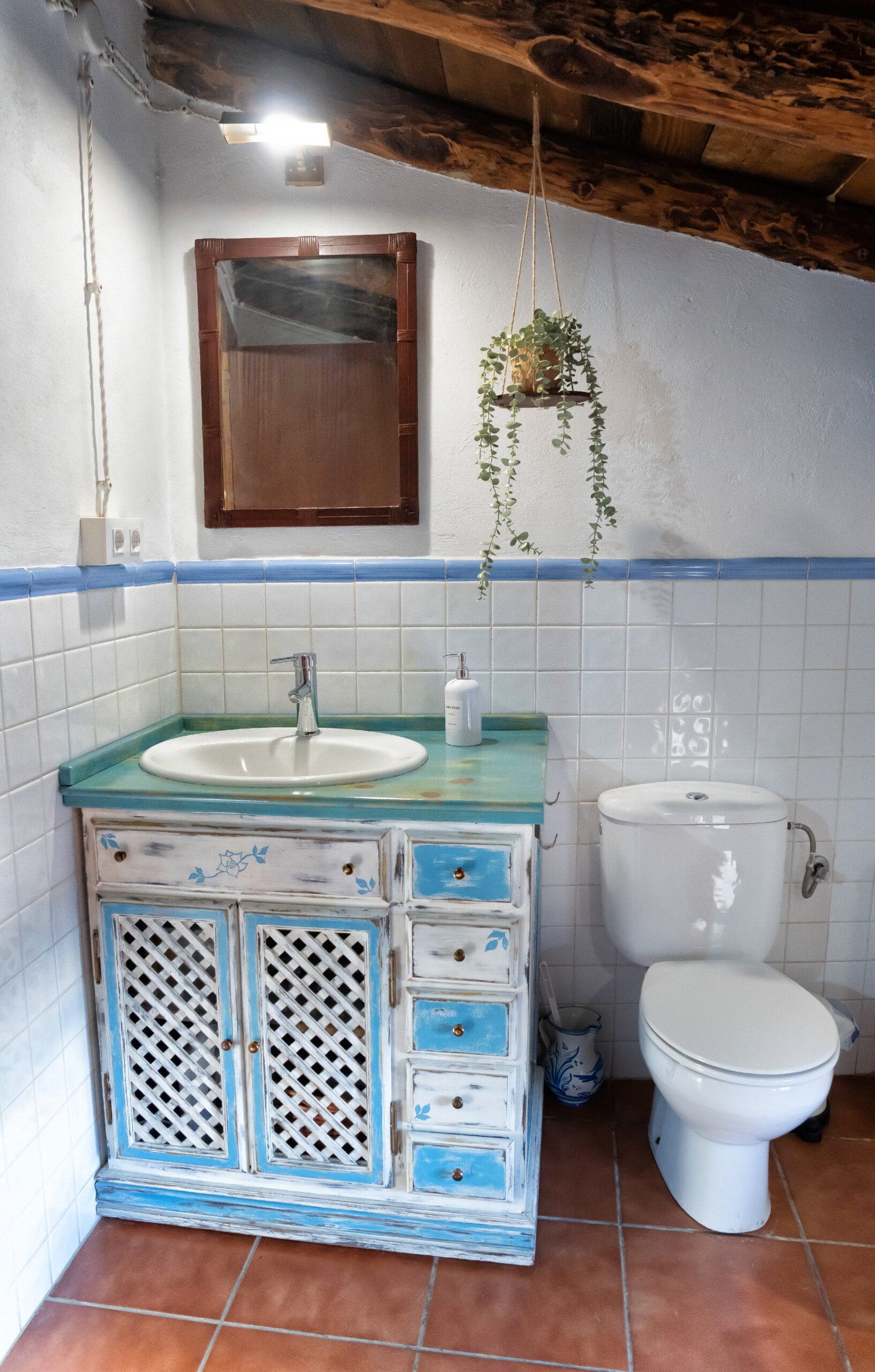 Baño completo con detalles tradicionales y mueble de lavabo artesanal. Baño rústico con lavabo en mueble artesanal azul y blanco, inodoro y detalles de madera en Mirador de Santa Ana.